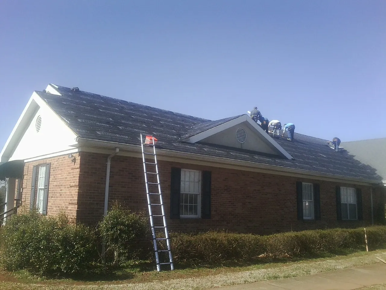 Crew tearing shingles off a brick ranch roof with a ladder set — Metal Roof Repair work by our crew in Shokan