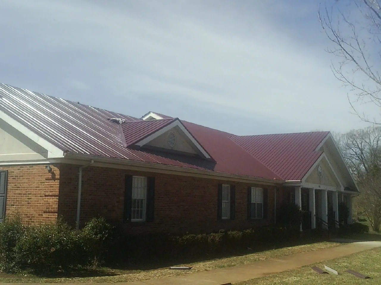 Red metal roof with gabled entries on a long brick building, from a Hail Damage Roof Repair job in Shokan