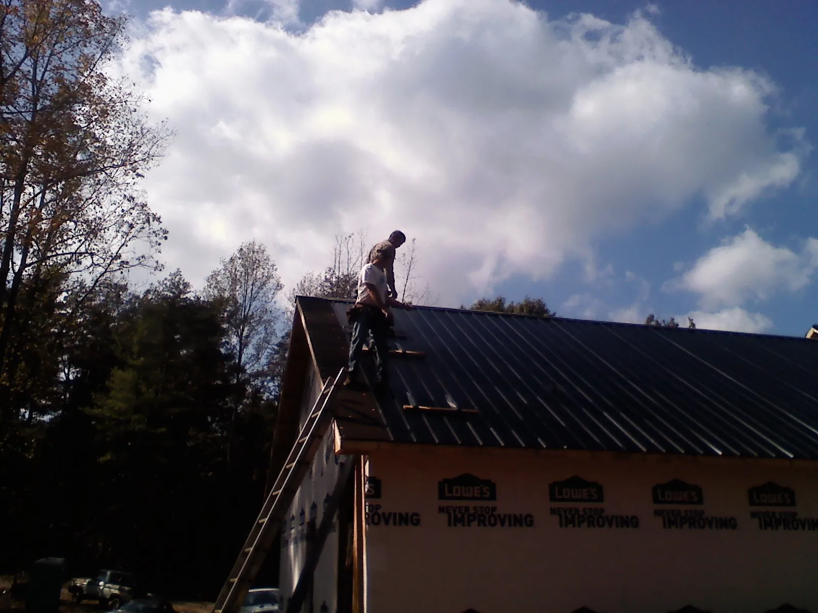 Roofer fastening dark metal panels high against a cloudy sky, from a Roof Inspection job in Shokan