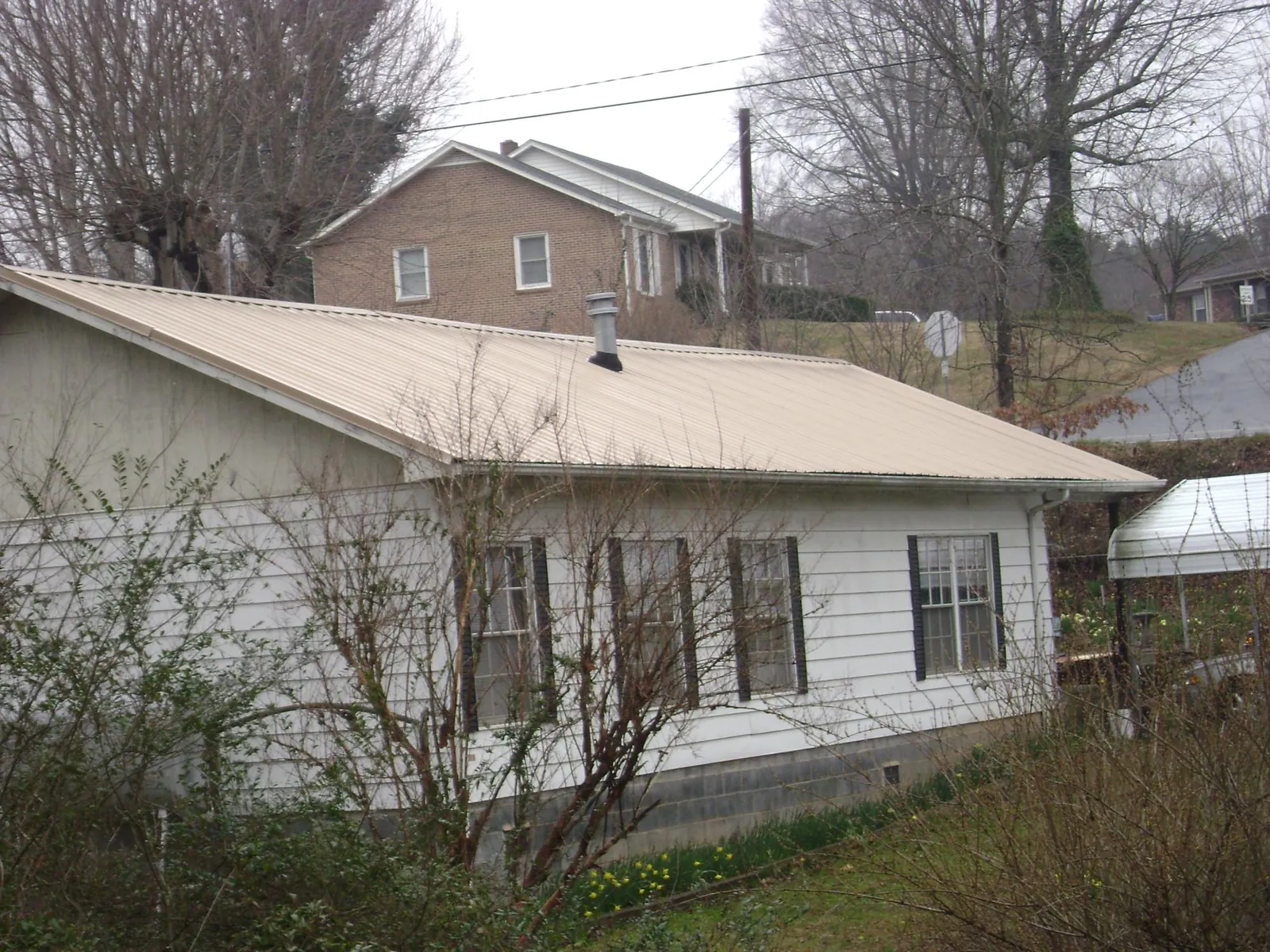 Tan metal roof on a white sided house set into a hillside — Commercial Roofing by Roofing Brothers in Shokan